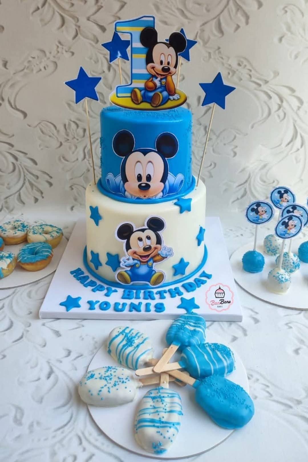 Toddler with frosting smeared across cheeks grinning at a birthday cake
